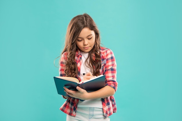 Ernstes Teenager-Mädchen macht sich Notizen zur Ausbildung auf blauem Hintergrund