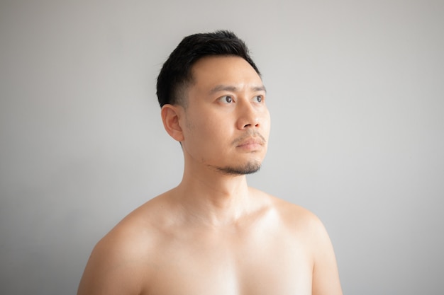 Ernstes und Druckgesicht des asiatischen Mannes im topless Portrait lokalisiert auf grauem Hintergrund.