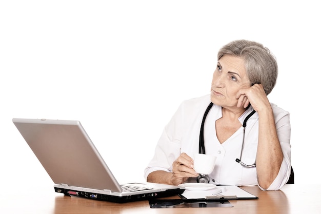 Ernsthafte ältere Ärztin, die mit Computer am Tisch sitzt