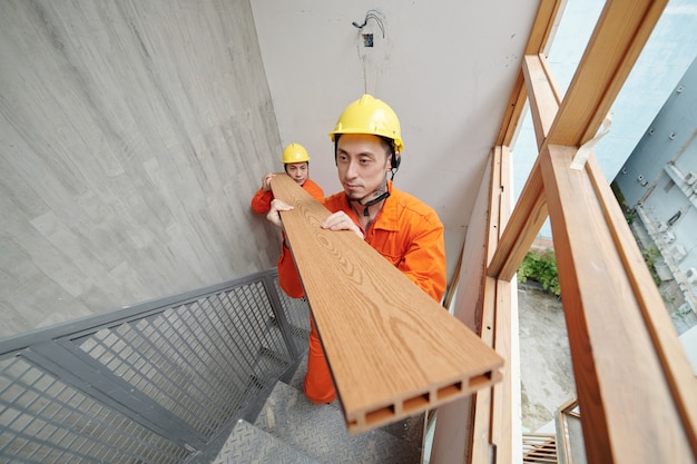 Ernsthafte Bauarbeiter, die Baumaterialien in die obere Etage des Hauses tragen