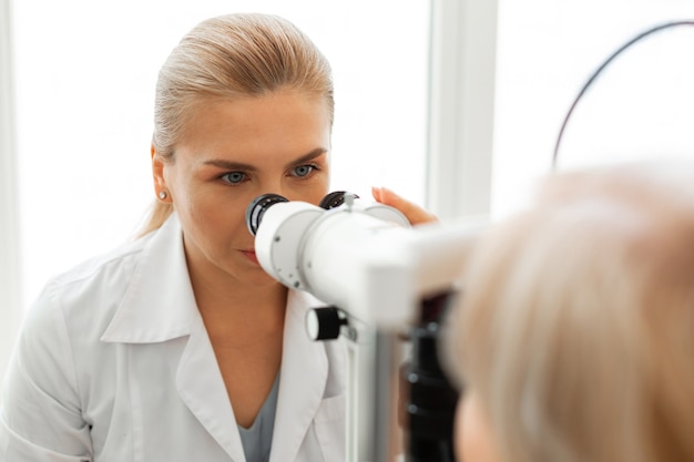 Ernsthafte blonde Dame mit blauen Augen als professioneller Augenarzt