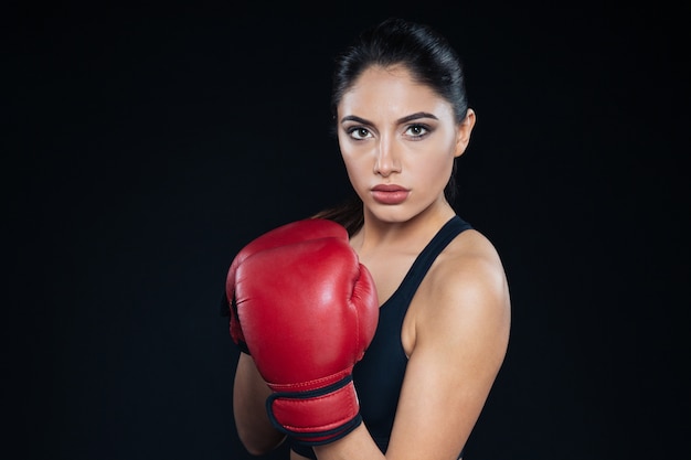 Ernsthafte Fitnessfrau in Boxhandschuhen mit Blick in die Kamera auf schwarzem Hintergrund
