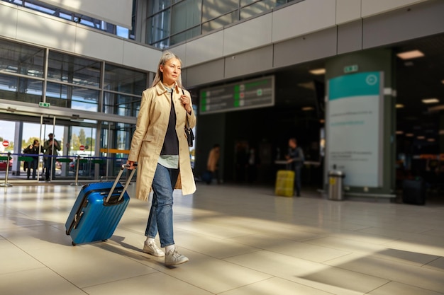 Ernsthafte Frau mit Reisetasche, die vor dem Flug das Flughafenterminal hinuntergeht