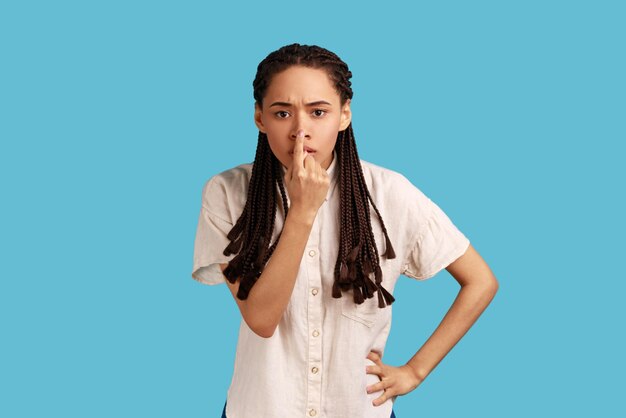 Foto ernsthafte frau mit schwarzen dreadlocks, die mit dem finger auf der nase steht und eine lügengeste zeigt