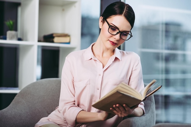 Ernsthafte Geschäftsfrau, die das Buch liest und im Sessel sitzt