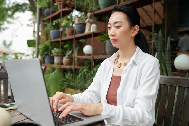 Ernsthafte Geschäftsfrau in weißem Hemd arbeitet am Laptop in einem Café