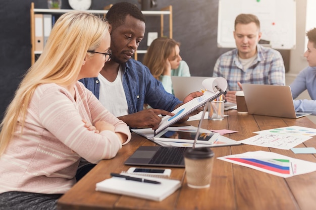 Ernsthafte Geschäftspartner, die im modernen Büro arbeiten. Zwei besorgte multiethnische Mitarbeiter diskutieren über ein neues Projekt, während sie am Laptop arbeiten, Platz kopieren