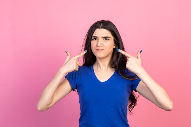 Ernsthafte junge Dame, die mit den Fingern auf sich selbst zeigt und auf rosa Hintergrund steht Hochwertiges Foto