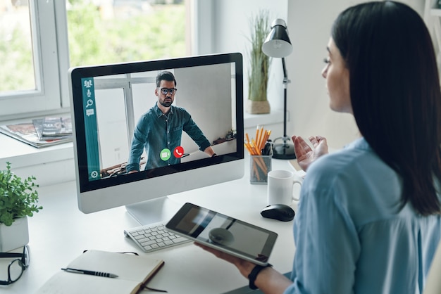 Ernsthafte junge Frau, die mit einem Kollegen per Videoanruf spricht, während sie im Büro sitzt