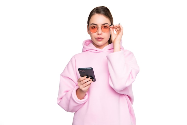 Ernsthafte junge Frau in lässigem rosa Hoodie, die eine Brille mit Smartphone-Handy anpasst