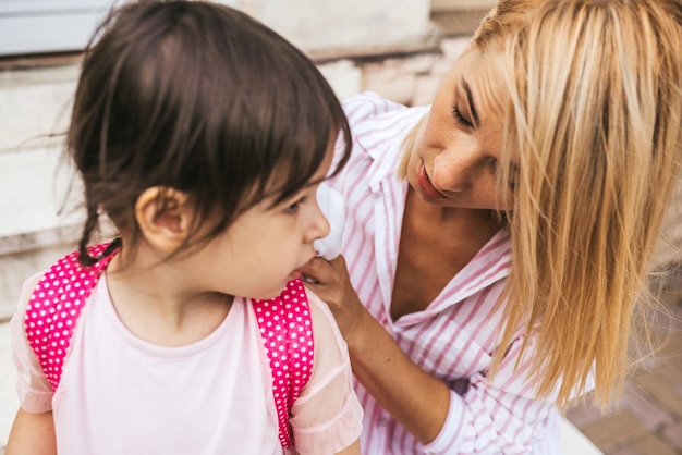 Ernsthafte Mutter und Schülertochter, die den Rucksack für den Besuch der Vorschule vorbereitet, sitzt auf der Treppe des Hauses im Freien Beziehungsunterstützung Süßes kleines Mädchen, das ihrer Mutter vor dem Vorschultag zuhört