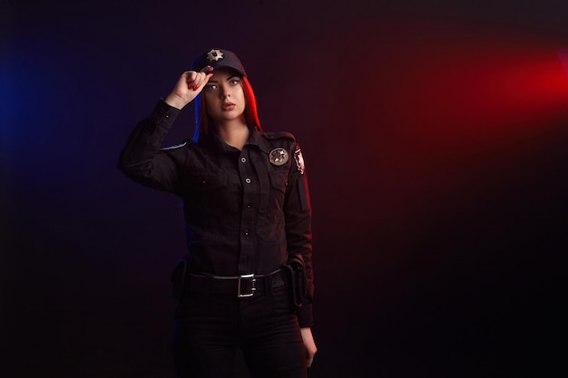 Ernsthafte Polizistin posiert für die Kamera vor schwarzem Hintergrund mit roten und blauen ...