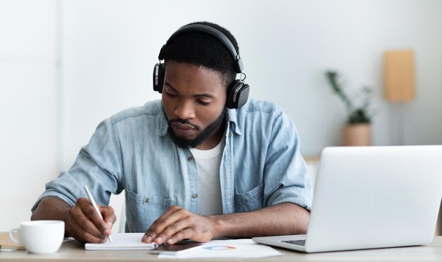 Ernsthafter afrikanisch-amerikanischer Student in Kopfhörern, der online Fremdsprachen lernt