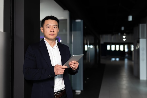 Ernsthafter asiatischer männlicher Arbeiter, der sich auf die Arbeit mit Tablet-Computern im modernen Büro konzentriert