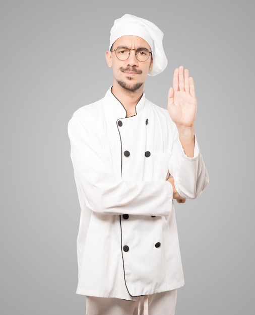 Ernsthafter junger Koch, der mit seiner Handfläche eine Geste des Stopps macht