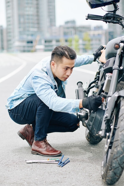 Ernsthafter junger Vietnamesen, der ein Problem mit dem Motorrad hat, repariert es auf der Straße
