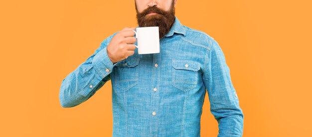 Foto ernsthafter kaukasischer mann hält einen teebecher mit gelbem hintergrund.