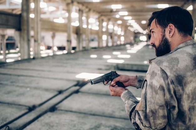 Ernsthafter Mann steht im Hangar und hält Paintballpistole in Händen.