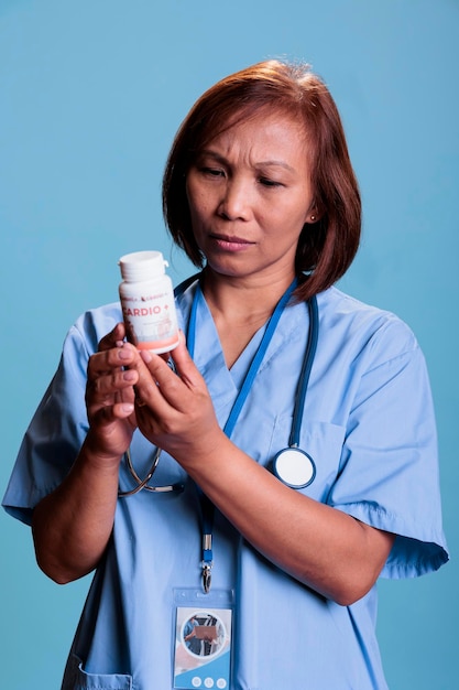 Ernsthafter medizinischer Assistent, der an der medikamentösen Behandlung arbeitet, um Patientenkrankheiten vorzubeugen, und eine Medikamentenbox hält, die eine pharmazeutische Packungsbeilage im Studio mit blauem Hintergrund liest. Gesundheitsdienst und Konzept