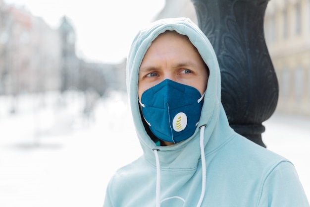 Ernsthafter nachdenklicher Mann trägt Hoodie und Atemschutzmaske beim Gehen auf der Straße, schützt vor Infektionen mit Influenzaviren oder Coronaviren, vermeidet überfüllte Orte in der Öffentlichkeit und kümmert sich um die Gesundheit