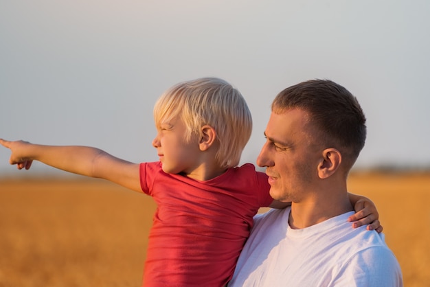 Ernsthafter nachdenklicher Vater hält Sohn in den Armen und schaut in die Ferne. Wochenende auf dem Land