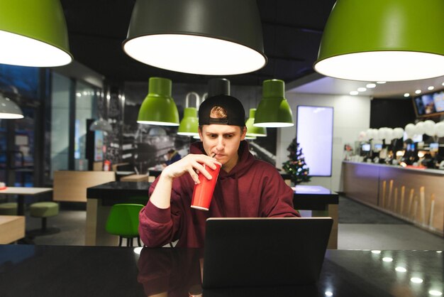 Ernsthafter Teenager benutzt einen Laptop für eine Pause in einem Fast-Food-Restaurant