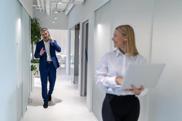 Ernsthafter Unternehmer telefoniert beim Gehen auf seinen Geschäftspartner entlang des Bürokorridors