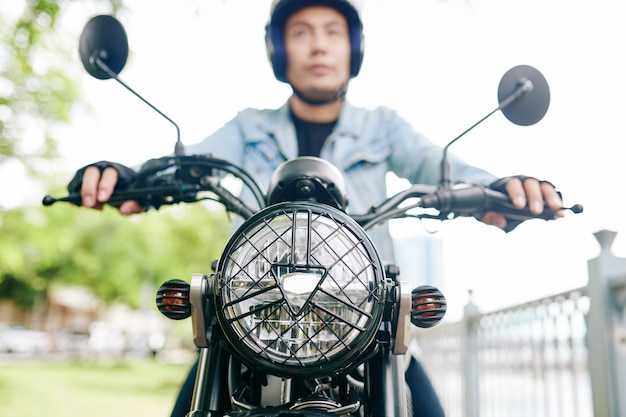 Ernsthafter vietnamesischer Mann im Helm, der auf Motorrad fährt, Fokus auf Scheinwerfer