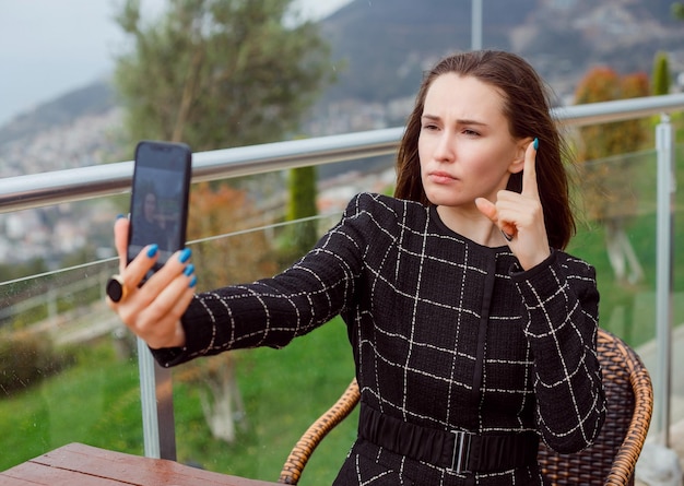 Foto ernsthaftes blogger-mädchen macht ein selfie mit der rückkamera des smartphones, indem sie ihren zeigefinger auf dem hintergrund der naturansicht zeigt