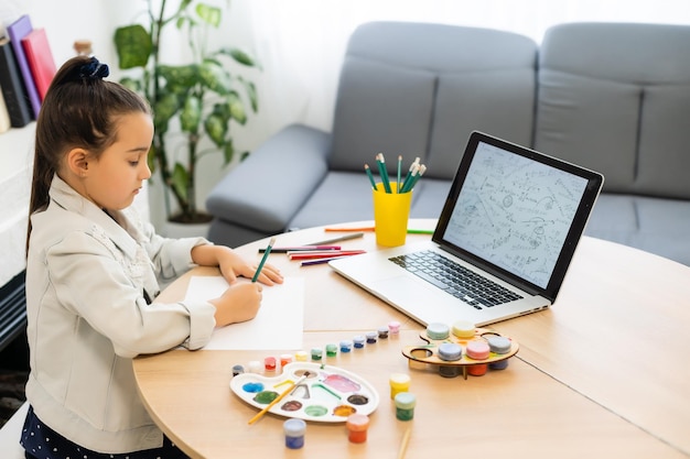 Ernsthaftes kleines Mädchen in Kopfhörern handschriftlich studieren online mit Laptop zu Hause, süßes, glückliches kleines Kind nimmt Internet-Web-Unterricht oder Unterricht auf dem PC.