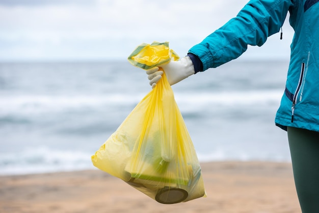 Ernte nicht erkennbare Aktivistin, die Tasche mit gesammeltem Müll an der Küste zeigt