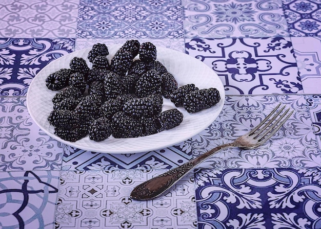 Ernte reifer Brombeeren auf einem weißen Teller auf blauem Vintage-Hintergrund