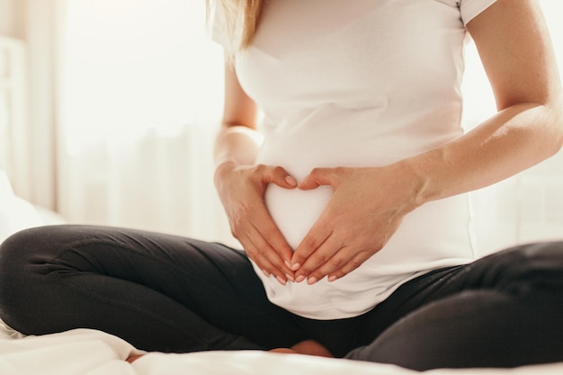 Ernte schwangere Frau, die Herzgeste auf ihrem Bauch zeigt