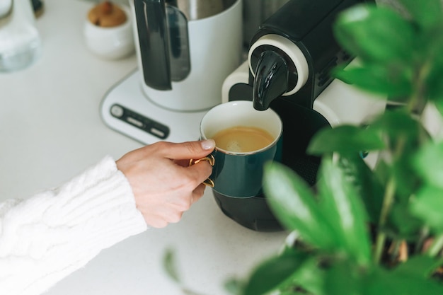 Erntefoto einer jungen Frau, die in der Küche des Hauses Kaffee aus der Kaffeemaschine gießt