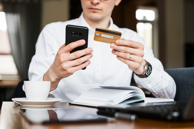 Ernten Sie männliche Hände unter Verwendung eines Smartphones und einer goldenen Kreditkarte, die in einem Café sitzen.