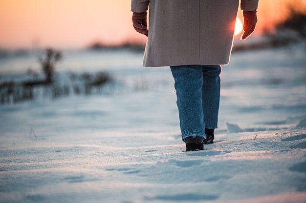 Ernten Sie unerkennbare Frau in warmen Kleidern und Stiefeln auf frischem weißem Schnee in der Winterlandschaft zur Sonnenuntergangszeit