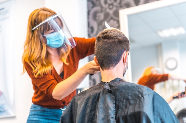 Eröffnung von Friseursalons nach der Coronavirus-Pandemie, covid-19. Sicherheitsmaßnahmen, Gesichtsmaske, Schutzschirm, soziale Distanz. Friseure in der neuen Normalität