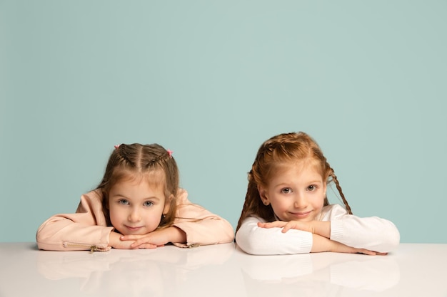 Erröten. Glückliche Kinder, Mädchen auf blauem Studiohintergrund isoliert. Schauen Sie glücklich, fröhlich. Exemplar für Anzeige. Kindheit, Bildung, Emotionen, Gesichtsausdruckkonzept. Am Tisch sitzen, süß.