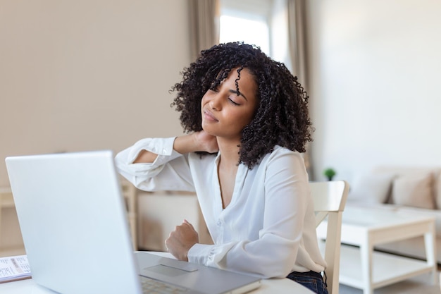 Erschöpft fühlen Frustrierte junge Frau sieht erschöpft aus und massiert ihren Hals, während sie an ihrem Arbeitsplatz sitzt