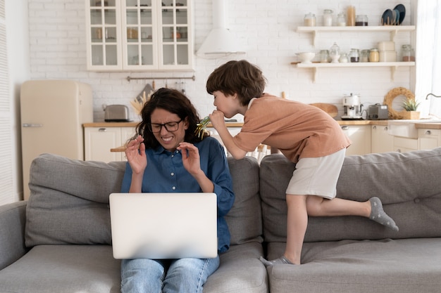 Erschöpfte alleinerziehende mutter arbeitet von zu hause aus mit einem sturen kleinen vorschulsohn vom laptop aus