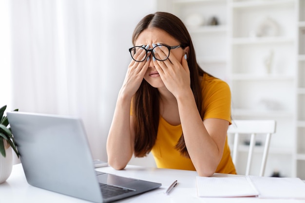 Foto erschöpfte asiatische frau reibt sich müde augen und leidet unter überanstrengung der augen, nachdem sie einen laptop benutzt hat