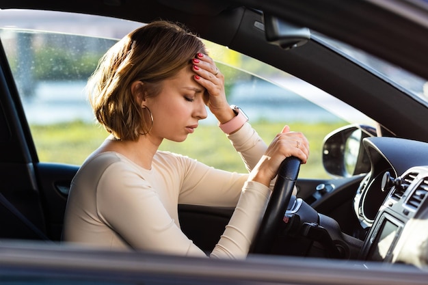 Erschöpfte Fahrerin hat Kopfschmerzen, sitzt im Auto, hält die Hand am Kopf und fühlt sich ängstlich