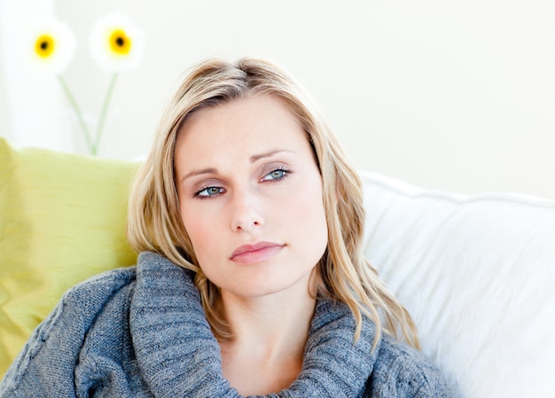 Erschöpfte Frau, die auf dem Sofa mit einem grauen Pullover liegt