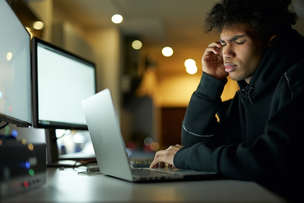 Erschöpfung müder junger Mann, der Kopfschmerzen hat, nachdem er zu lange am Laptop gearbeitet hat, der mit den Augen sitzt