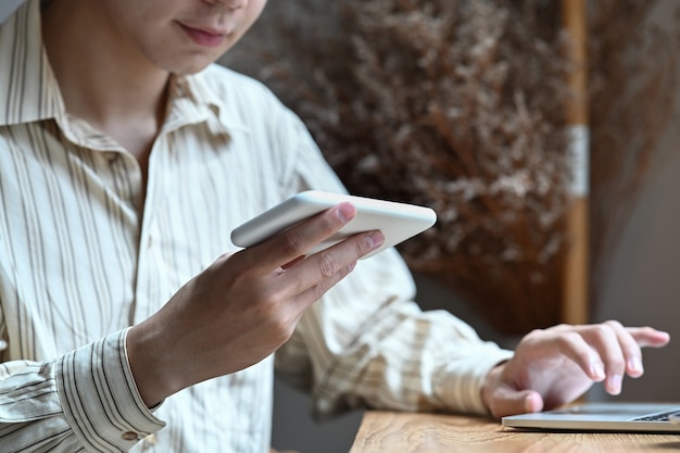 Erschossener lächelnder Mann, der Handy hält und mit Laptop-Computer arbeitet.