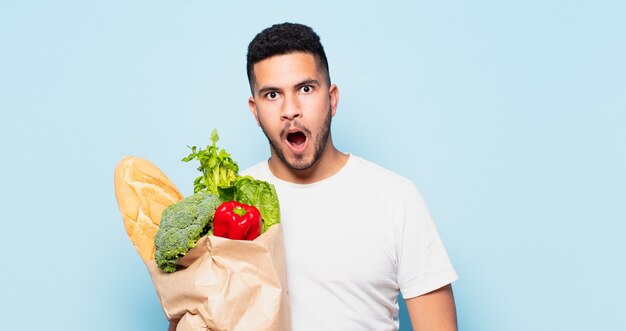 Erschrockener Ausdruck des jungen hispanischen Mannes Einkaufsgemüse-Konzept