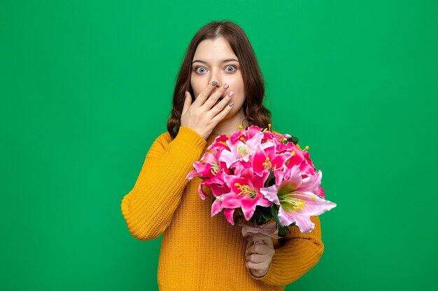 Erschrockener bedeckter mund mit dem schönen jungen mädchen der hand, das blumenstrauß hält