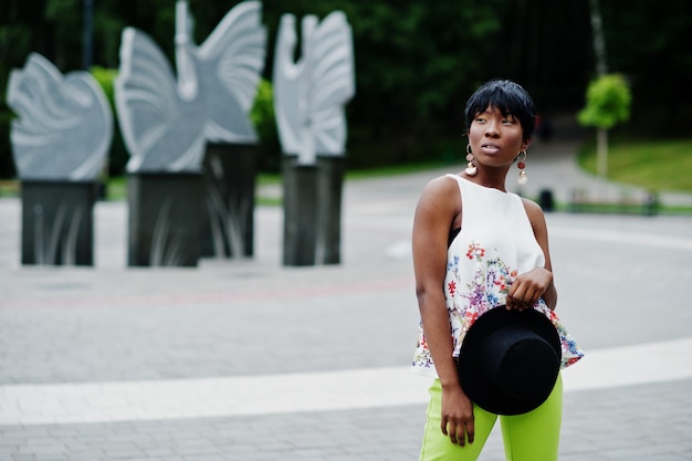 Erstaunliche afroamerikanische Modellfrau in grüner Hose und schwarzem Hut posierte im Park
