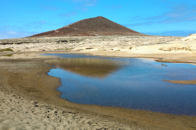 Erstaunliche Ansicht des Vulkans Montana Roja mit Teich im Naturreservat der Sandwüste von El Medano, Teneriffa, Spanien