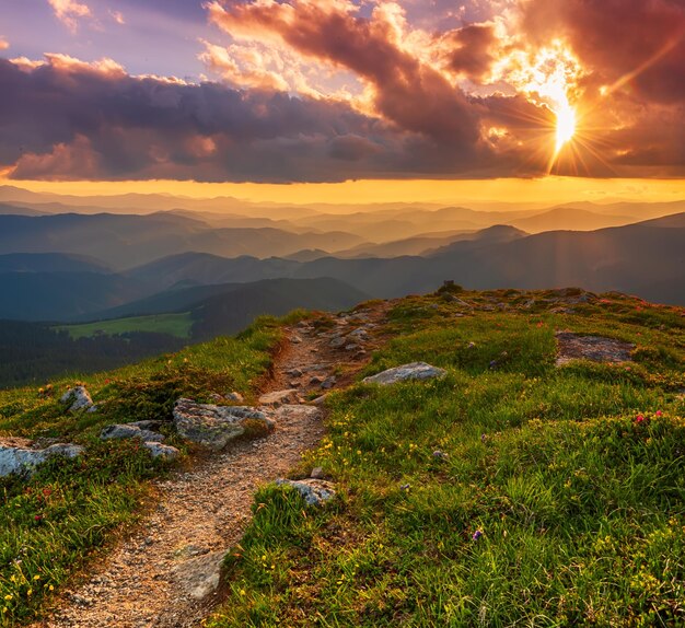 Erstaunliche Berglandschaft mit farbenfrohem, lebendigem Sonnenuntergang am bewölkten Himmel und Weg durch die Felsen, natürlicher Reisehintergrund im Freien. Schönheitswelt.